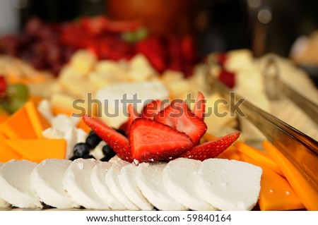 Tray of sliced cheeses and fruits, selective focus on the sliced strawberries