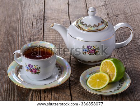 A cup of tea with lemon and tea maker on wood background