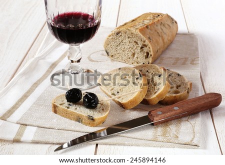 French bread with olives and Provencal olives on a wooden cutting board and glass of red wine