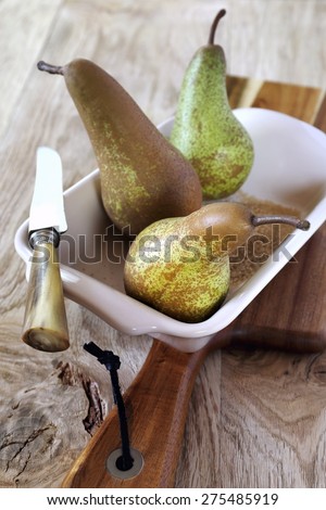 Three pears Conference in ceramic baking dish, brown sugar and vintage knife on wooden cutting board