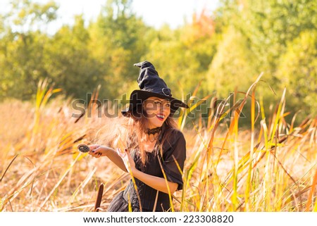 smiling young long haired woman wearing black dress, black corset and witch hat, paddle brush in hands