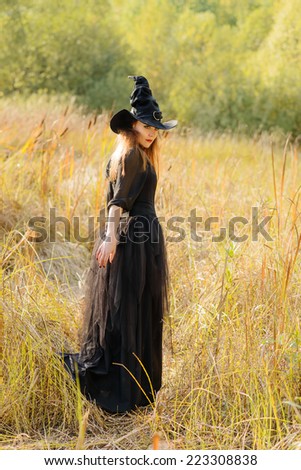 young long haired woman wearing black dress, black corset and witch\'s hat, looking away with arm extended downward