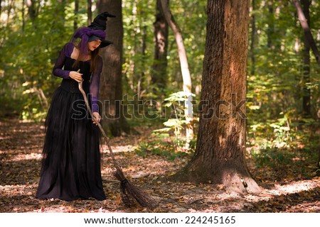 young woman in witch\'s hat holding broom and looking downwards, sweeping leaves