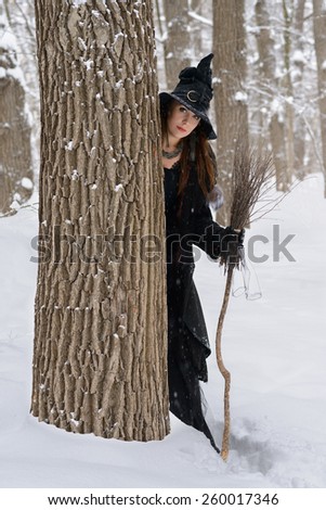 Woman in witch's hat holding broom in winter forest