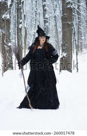 Woman in witch\'s hat holding broom in winter forest