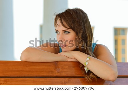 Young smiling woman looking away and resting chin on palm, leaning on bench.