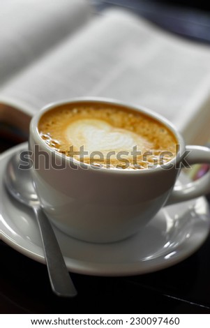 A close up view of a cup of latte with the bible behind it.
