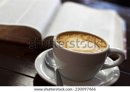 A close up view of a cup of latte with the bible behind it.
