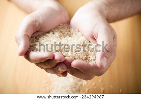 A pair of hands holding rice grains in a tabletop