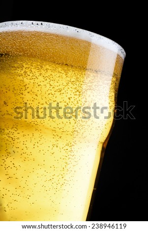 A topped off beer pint over a black background