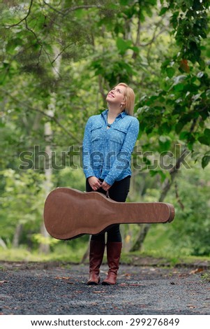 A young musician woman in an outdoor setting with a guitar case and guitar.