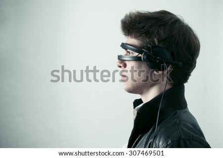 A profile portrait of a young man with a pair of headphones placed in a way to cover his eyes like a futuristic set of sunglasses