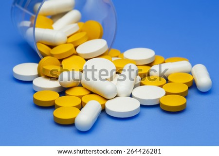 Pills and capsules spilling from a medicine cup.
