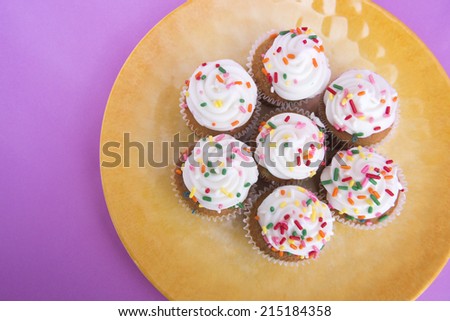 Mini cupcakes on yellow plate with pink/purple background