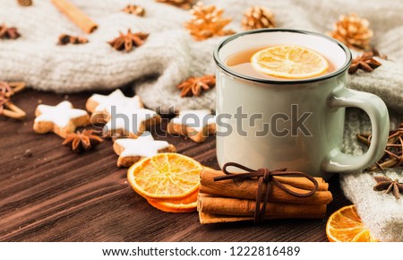 Winter and New Year theme. Christmas tea with spices, cup of tea with orange, cinnamon, anise, cookies in a shape of star, fir cones, pepper and gray scarf on wooden background. Copy space for text.