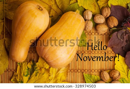 Words hello november on the rustic background with maple leaves, walnuts and two pumpkins