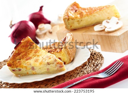 Fresh home baked quiche on a plate and chopping board with fork, napkin, onions and mushrooms