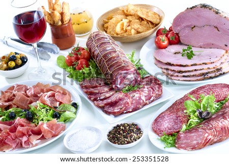 Fresh organic charcuterie display showing cold sliced meats, garnish, savory snacks, oil dressing, salt and pepper and red wine drink
