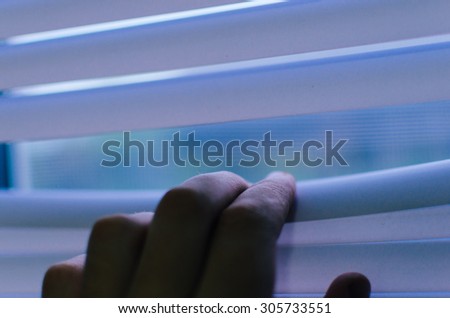 Hand separating slats of venetian blinds with a finger to see through