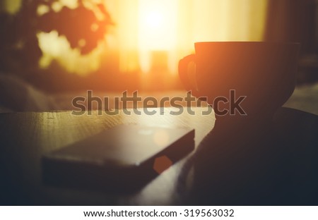 Cup of coffe or tea with phone on the home bedroom wood table in sunset time with soft light