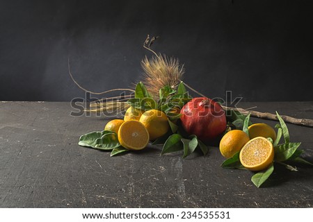 Composition of oranges, leaves, pomegranate, branch and ears on a grunge wooden table and a black background.