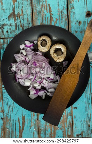 Mushroom and onion in black pan on kitchen blue table