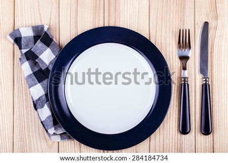 Empty dish, knife and fork and blue napkin on wood table