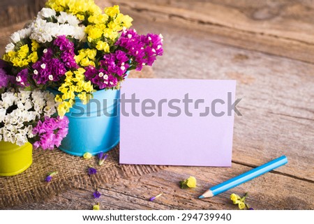 Dried flowers in brightly colored buckets with a pencil and a card on a wooden background