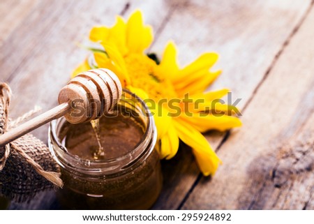 A jar of honey with sunflowers and spoon on old wooden backgroun