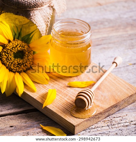 A jar of honey with sunflowers and spoon on old wooden background