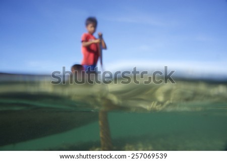 Blurry and soft focus of kid in a wooden boat at the sea with blue sky and underwater scenery