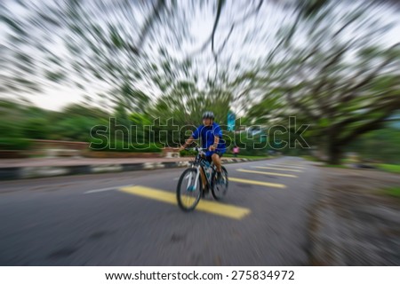 A blurry image with zooming effect of a man cycle a bike at park with tree surrounding the area