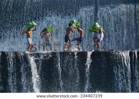 Boys were having fun by playing water in an artificial dam on the Tukad Unda dam, Bali, Indonesia. Bali island is a popular tourist destination in the world. Happiness, joyfull, friendship concept