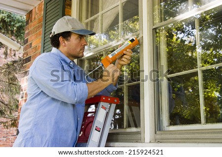 Man on ladder caulking outside window