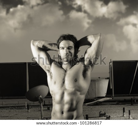 Fine art sepia toned portrait of hunky male fitness model posing against dramatic cloudscape sky