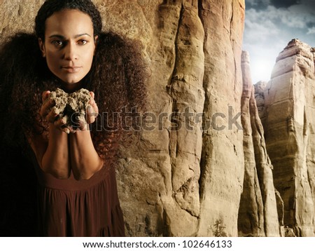 Unique portrait of a woman holding dirt in her hands close to body in brown dress against background of majestic cliff scene