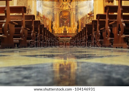 Interior of a beautiful old catholic church from below with marble floor, wooden pews, and light streaming onto altar with Jesus on crucifix