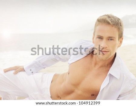 Successful young good-looking guy on the beach with relaxed open shirt