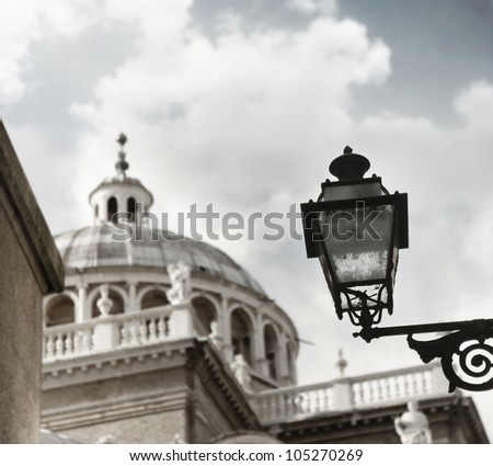 Very old iron and glass lamp in foreground with large renaissance dome and skyscape in background