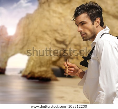 Sexy masculine man in formal clothes smoking cigar on exotic beach