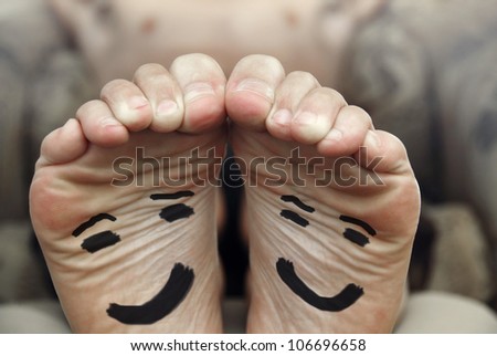 Funny image of a pair of bare male feet with happy smiley face drawn on bottom