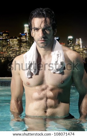 Sexy male model with great abs and muscular body in swimming pool at night with city skyline background