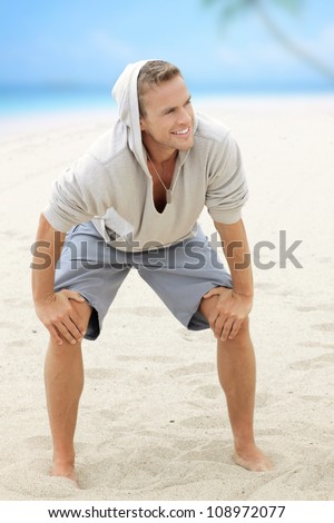 Young happy guy having fun on the beach with nice smile and barefeet in the sand
