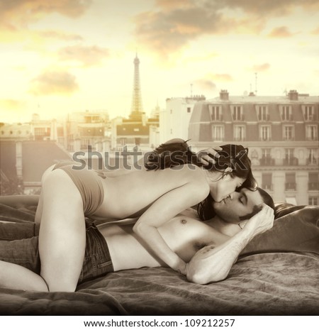 Young sexy couple making passionate love in bed against window overlooking Paris skyline with retro vintage sepia tones