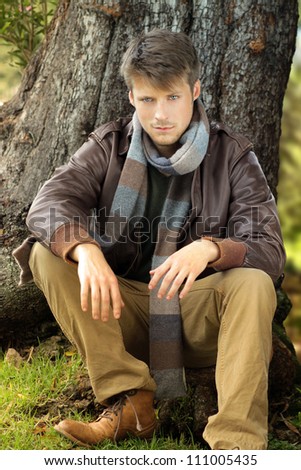 Young handsome man outdoors in fall clothing against tree