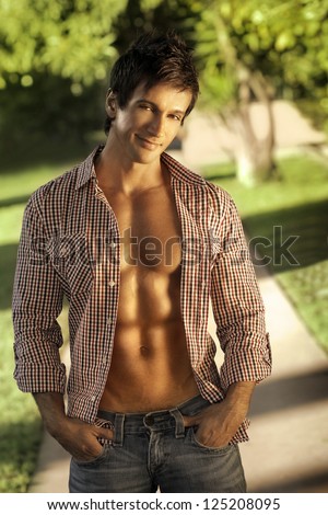 Fashion portrait of a handsome man with open shirt and muscular abs outdoors