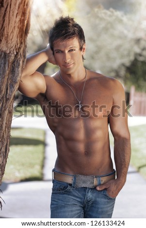 Portrait of a beautiful young muscular man leaning against a tree in nature