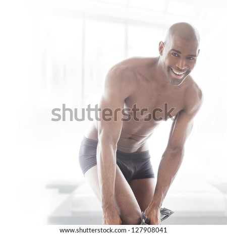 Intimate fun portrait of a young fit man putting his pants on with great smile