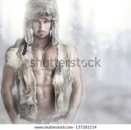 Fashion portrait of a beautiful male model in fur hat and vest against modern background with copy space