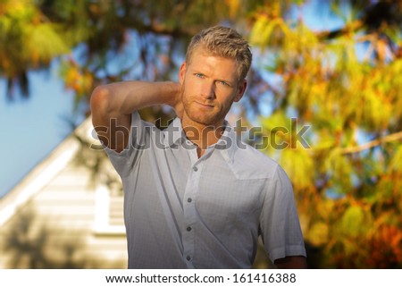 Attractive young man standing outside in front of house with big tree blurred in background